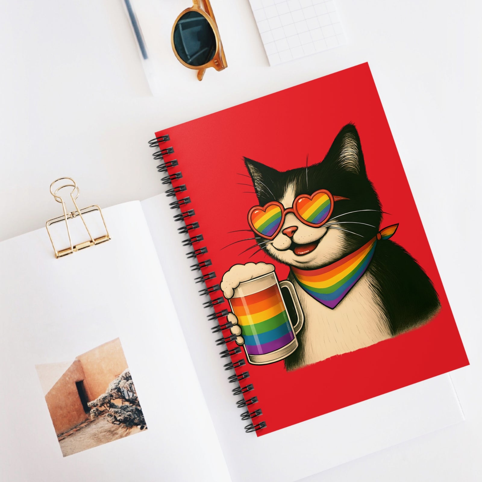 Notebook with a cat illustration holding a rainbow mug on a white surface